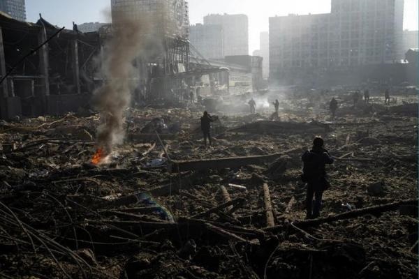 Pessoas se reúnem em meio à destruição após o bombardeio de um shopping center, em Kiev, Ucrânia [Rodrigo Abd/AP Photo]