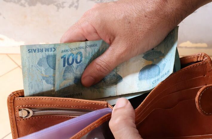 Mão movimenta cédulas de R$ 100 no interior de uma carteira de couro. Foto: Álvaro Rezende