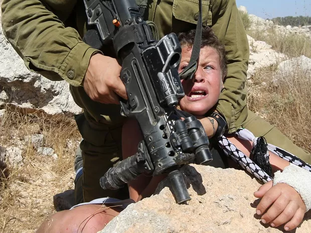 Soldado armado ameça um menino palestino durante massacre do exército de Israel a manifestantes palestinos ocorrido depois de marcha contra o confisco de terras palestinas para expandir assentamentos judeus em Nabi Saleh, Cisjordânia.