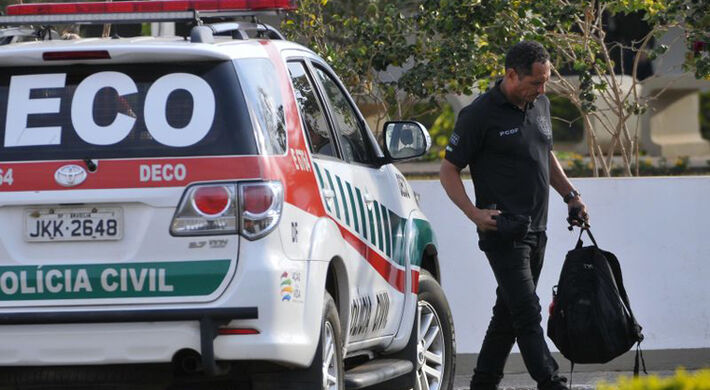 Policial ao lado de viatura durante Operação Panoptes: fraude em concursos liderada por Helio Ortiz