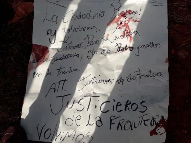 Cartaz deixado por “Justiceiros da Fronteira” ao lado de corpo