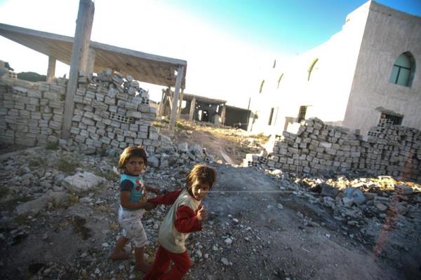 Crianças caminham entre área destruída por ataques de 11 de maio em Guta oriental.
