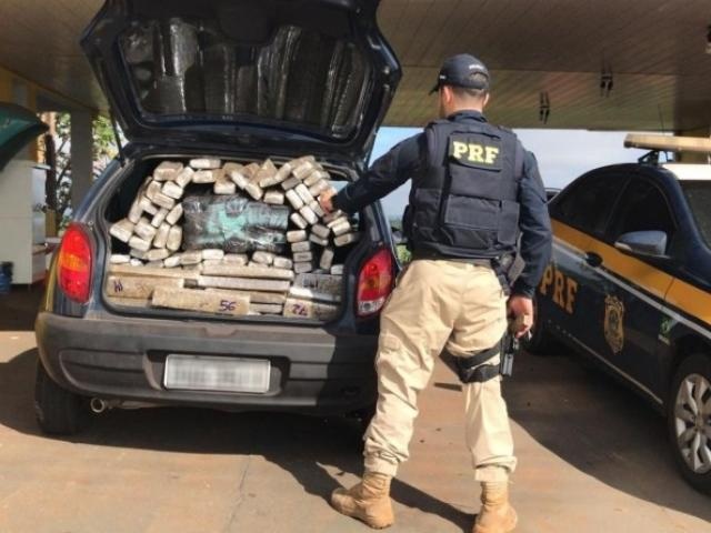 Policial contando a quantidade de tabletes de droga encontrados no porta-malas do veículo