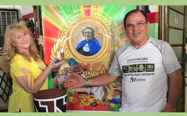 Sylvia Cesco e Moacir Lacerda diante de um quadro com a foto de Glorinha Sá Rosa