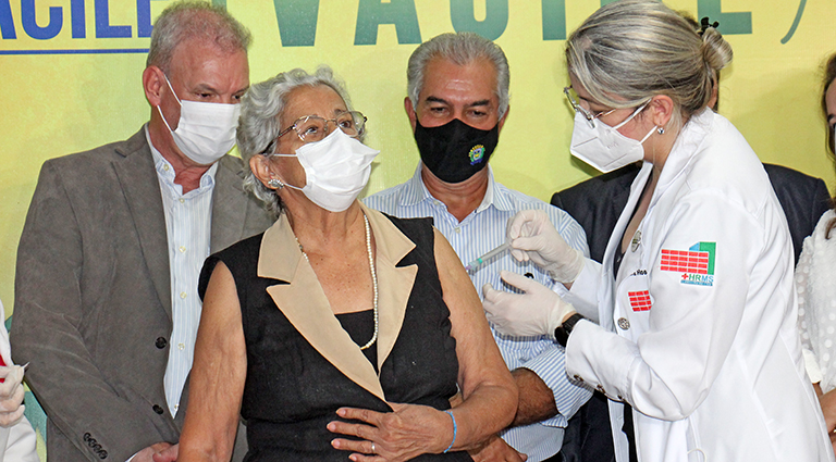 Maria recebendo a 1ª dose acompanhada do governador Reinaldo Azambuja e do secretário Geraldo Resende, em 18 de janeiro de 2020. (Foto: Chico Ribeiro)