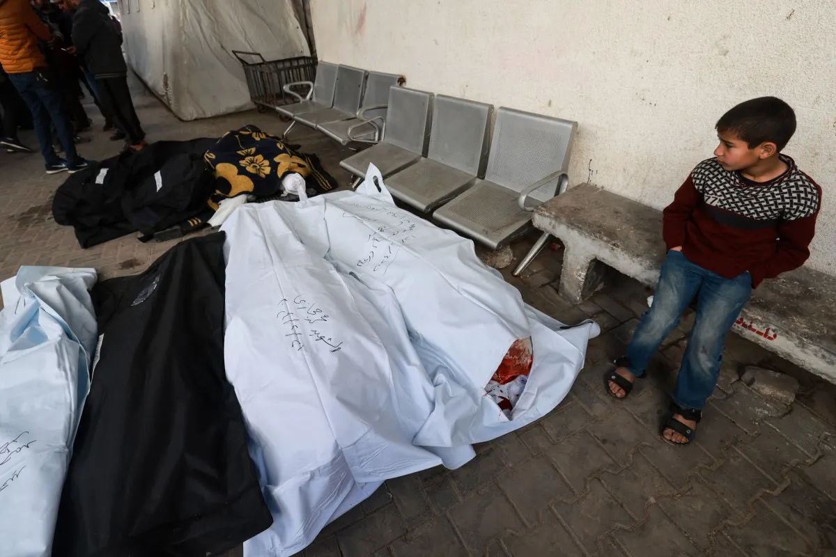 Um menino palestino olha para os corpos no Hospital al-Najjar. [Mohammed Abed/AFP]